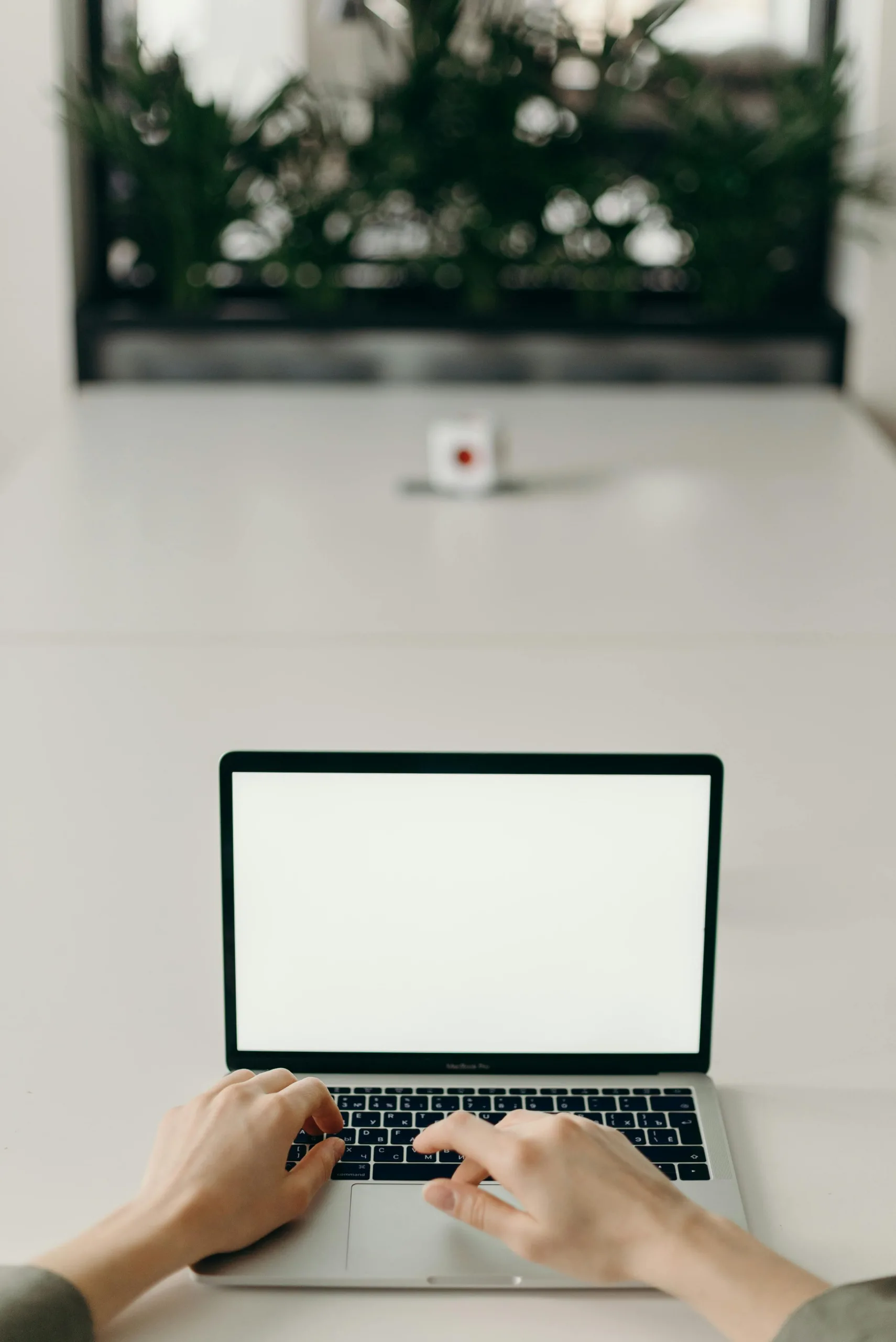 Hands typing on a laptop with a blank screen in a minimalist workspace.